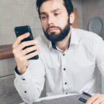 A man looks frustrated while checking his smartphone, possibly experiencing a banking issue or scam.