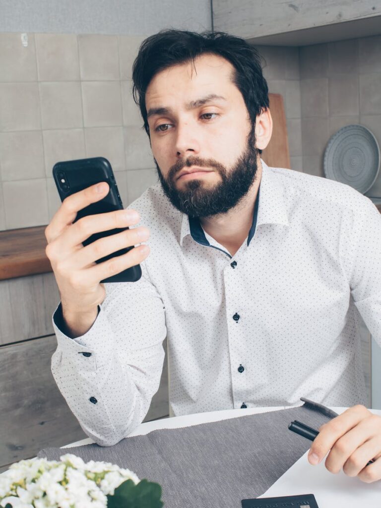 A man looks frustrated while checking his smartphone, possibly experiencing a banking issue or scam.