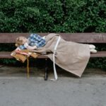 A woman sleeping wrapped in a blanket on a park bench, illustrating homelessness and solitude.