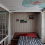 A small bedroom with a unique ceiling design, featuring water stains and an eclectic bed setup.