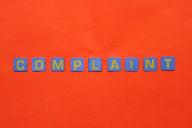 Blue letter tiles spelling 'COMPLAINT' on a vibrant red surface.
