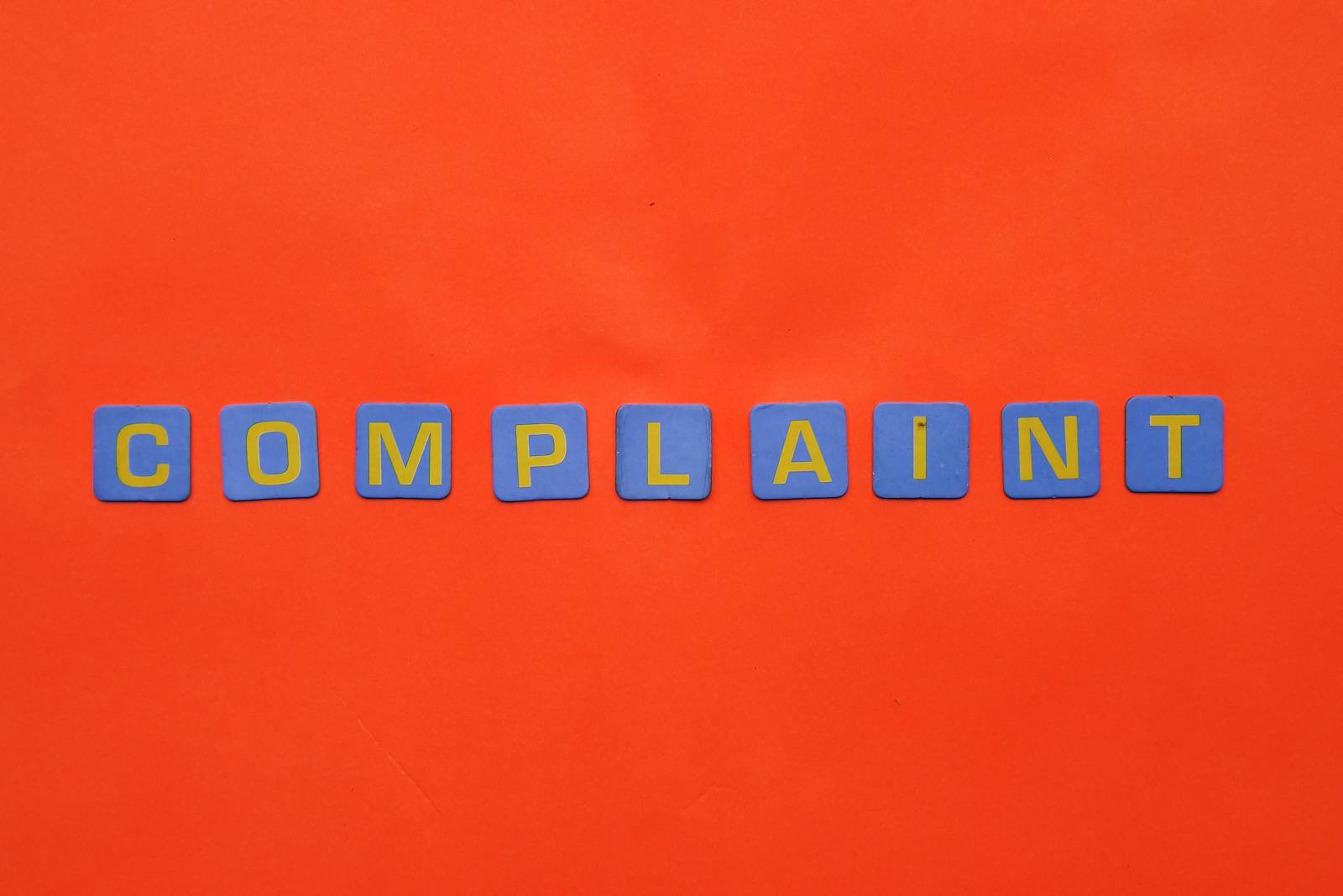 Blue letter tiles spelling 'COMPLAINT' on a vibrant red surface.