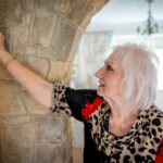 Elderly woman with gray hair adjusting temperature controller indoors.