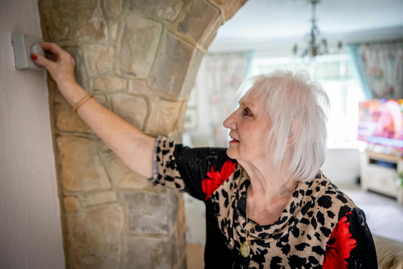 Elderly woman with gray hair adjusting temperature controller indoors.
